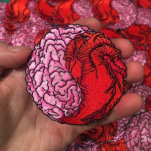May include: A pink and red embroidered patch of a brain and heart intertwined. The brain is pink and the heart is red.