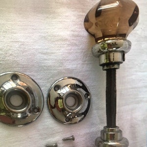 May include: A set of antique door hardware with a brown glass knob, two chrome escutcheons, and four screws.