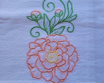 May include: A white fabric surface featuring an embroidered design of a large, multi-petaled peach-colored flower with a yellow center. Above the flower are green embroidered stems, leaves, and two small, rounded, peach-colored flower buds.