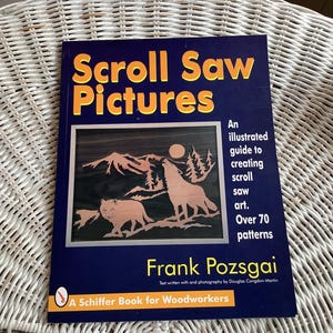 May include: A book titled "Scroll Saw Pictures" with a dark blue cover and orange lettering. The cover features a scroll saw art illustration of wolves and mountains. The book is a guide to creating scroll saw art with over 70 patterns.