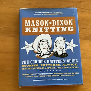 May include: A blue book with the title "Mason*Dixon Knitting: The Curious Knitters' Guide" by Kay Gardiner and Ann Shayene. The book cover features illustrations of two women wearing cowboy hats and the text "Stories. Patterns. Advice. Opinions. Questions. Answers. Jokes and Pictures."