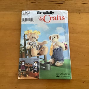May include: Simplicity Crafts pattern for making teddy bears. The cover features illustrations of teddy bears in various outfits, including overalls and floral accessories. The pattern is titled "Straw Stockings."