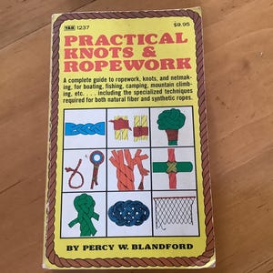 May include: A yellow book titled "Practical Knots & Ropework" with a brown rope border. The book cover features illustrations of different knots and ropework techniques. The book is by Percy W. Blandford.