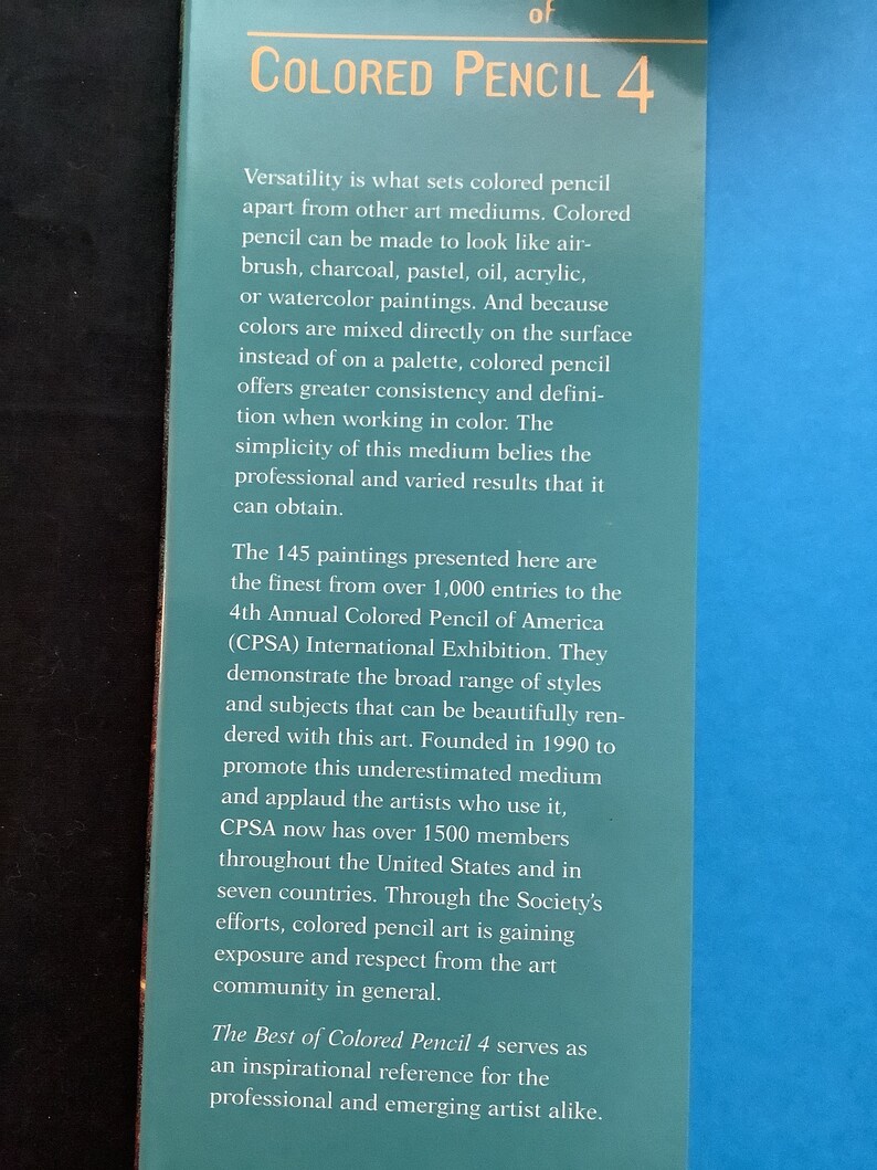 K&ouml;nnte beinhalten: Ein Buchcover mit blauem Hintergrund und dem Titel "Colored Pencil 4" in goldenen Buchstaben. Der Text beschreibt das Buch als eine Sammlung von 145 Gem&auml;lden aus &uuml;ber 1.000 Einsendungen zur 4. Internationalen Ausstellung der Colored Pencil of America (CPSA).