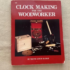 May include: A red book titled "CLOCK MAKING FOR THE WOODWORKER" with images of clock-making tools and a clock. The book cover features the title in white letters. The book is by Wayne Louis Kadar.