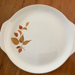 May include: White oval serving platter with a brown and orange leaf design. The platter has two handles.