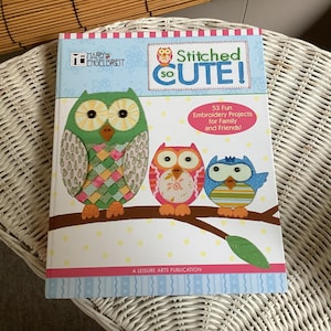 May include: A book titled "Stitched So Cute!" with a pink, white, and blue striped cover. The book features three embroidered owls, one green, one pink, and one blue, with a branch and leaves. The book cover states "53 Fun Embroidery Projects for Family and Friends!"