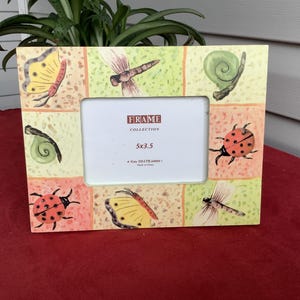 May include: A rectangular picture frame featuring a colorful border with illustrations of butterflies, dragonflies, ladybugs, and snails. The center insert displays the text FRAME COLLECTION 5x3.5, 4 Kids CO.LTD.2009, and Made in China.