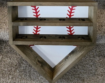 May include: A wooden baseball display shelf with two tiers and six slots for baseballs. The shelf is painted white with a red baseball stitch pattern. The shelf is shaped like a baseball diamond.