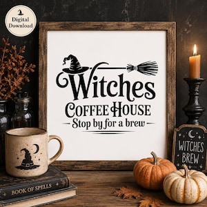 Pode incluir: Uma placa quadrada emoldurada com fundo branco e texto preto que diz Witches COFFEE HOUSE Stop by for a brew, com um gráfico de um chapéu de bruxa e uma vassoura. A placa é exibida ao lado de uma caneca de cerâmica, abóboras e livros.