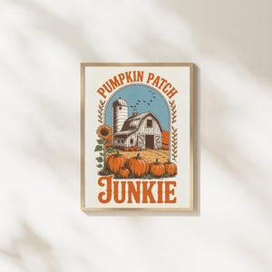 Könnte beinhalten: Gerahmter Druck mit einer Vintage-Illustration einer Scheune, eines Silos und Kürbissen. Die Worte "Pumpkin Patch Junkie" sind in orangefarbenem Text gehalten. Eine Sonnenblume und Vögel sind ebenfalls enthalten.