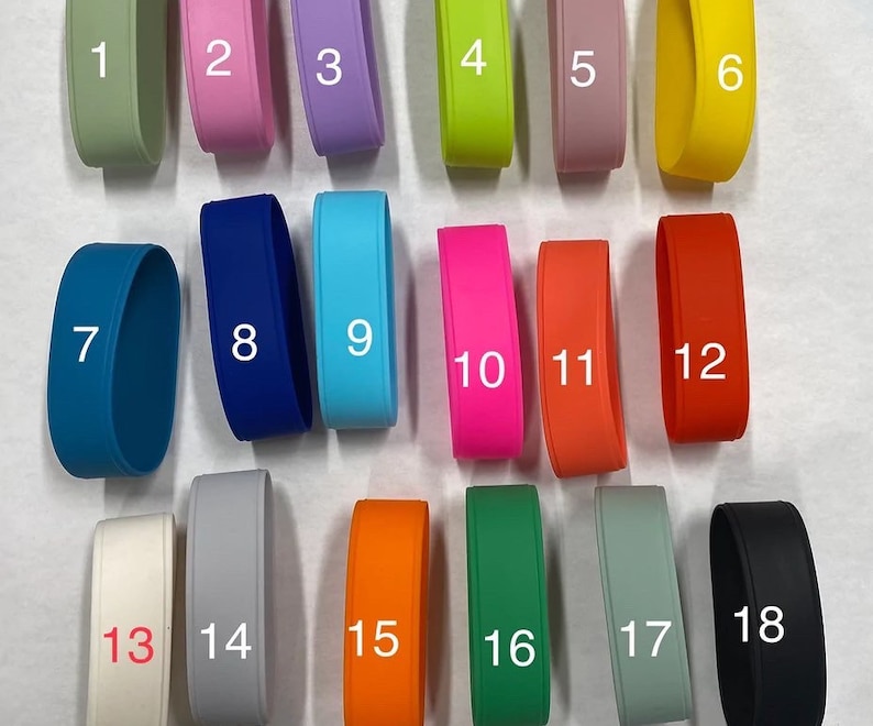 May include: A collection of eighteen silicone wristbands in various solid colors, each labeled with a white number from 1 to 18. The colors include shades of green, pink, purple, yellow, blue, orange, red, white, gray, and black in a matte finish.