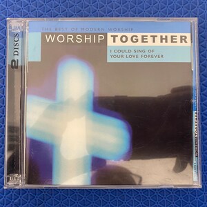 May include: A two-disc CD album titled Worship Together: The Best of Modern Worship, I Could Sing of Your Love Forever. The cover features a glowing, blurred light blue cross against a dark background, with white text on a light blue header.