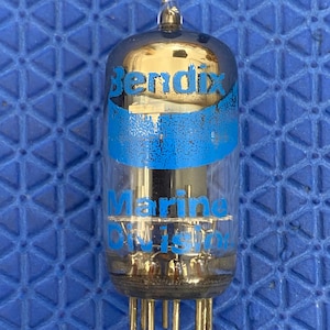 May include: A vintage Bendix Marine Division vacuum tube with a clear glass body and a metallic top. The tube has blue text that reads "Bendix" and "Marine Division". The tube has gold-coloured pins at the base.