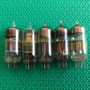 May include: Five vintage vacuum tubes with glass enclosures and metal pins. The tubes have a silver top and visible internal components. Some tubes have text that reads "RAYTHEON" and "SYLVANIA". The tubes are arranged in a row.