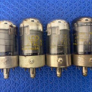 May include: Four vintage vacuum tubes with clear glass and silver tops. The tubes have a cylindrical shape with a metal base and multiple pins. The text "PHILCO" and "CRYSTAL" is visible on the tubes. Made in the U.S.A.
