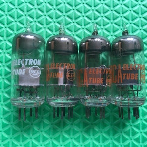 May include: Four vintage RCA Electron Tube vacuum tubes. Each tube is clear glass with a dark gray top and a series of pins at the base. The tubes have orange and white lettering.