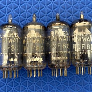 May include: Four vintage Philips Miniwatt vacuum tubes, each with a glass enclosure and multiple pins. The tubes are labeled with model numbers and the Philips brand name. The background is a blue textured surface.