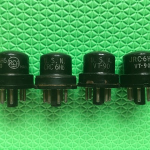 May include: Four black vacuum tubes with silver pins, each labeled with text including "6H6" and "VT-90". One tube has the "RCA" logo. The tubes are arranged in a row against a green textured background.