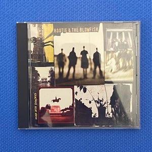 Könnte beinhalten: Eine Hootie & The Blowfish Cracked Rear View Musik-CD in einer transparenten Kunststoffhülle. Das Cover zeigt eine Collage aus Schwarz-Weiß-Fotos, darunter die Silhouetten von vier Personen, eine Reiterstatue und Bäume.