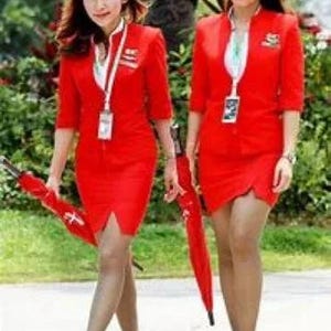 May include: Two women in matching red outfits, each holding a red umbrella. The outfits include a short-sleeved jacket and a skirt. They are wearing name tags and walking on a paved surface.
