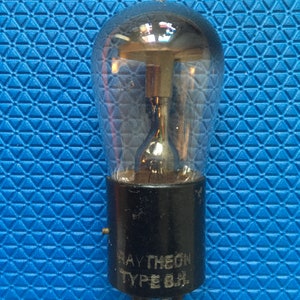 Puede incluir: Una válvula de vacío Raytheon Tipo 6B4 vintage. La bombilla de vidrio transparente tiene una parte superior redondeada con una punta. La base es negra con el logotipo de Raytheon y "TYPE 6B4" impreso en blanco. El tubo tiene varios pines de conexión.