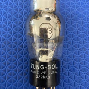May include: A vintage vacuum tube with a clear glass bulb and a black base. The tube has the text "TUNG-SOL MADE IN U.S.A." and "322NK3" printed on the base. The tube also has the number "83" visible.