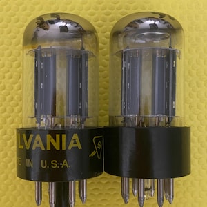 May include: Two vintage Sylvania vacuum tubes with clear glass bulbs and black bases. The tubes have multiple pins and the text "SYLVANIA" and "MADE IN U.S.A." is printed on the base.