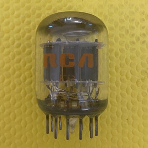 May include: A clear glass vacuum tube with the orange letters "RCA" visible. The tube has multiple internal components and metal pins at the base. The background is a textured yellow surface.