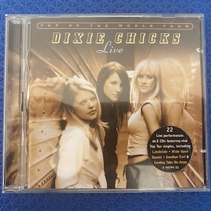 May include: Dixie Chicks "Top of the World Tour" live album on CD. The cover features a sepia-toned image of the band members. The album includes 22 live performances, including the songs "Landslide" and "Cowboy Take Me Away."