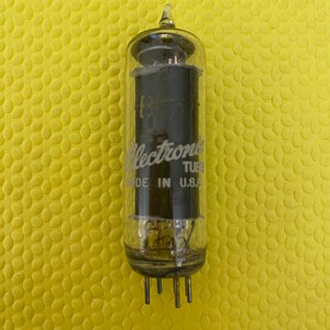 Puede incluir: Un tubo electrónico de vidrio transparente con el texto "Electronic Tube MADE IN U.S.A." impreso en el lateral. El tubo tiene forma cilíndrica con una parte superior puntiaguda y varios pines en la base. El fondo es una superficie amarilla texturizada.