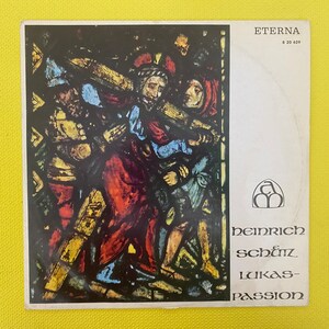May include: A vintage record album cover featuring a stained glass image of a religious scene. The album is titled "Heinrich Schütz Lukas-Passion" and is by the record label "Eterna".