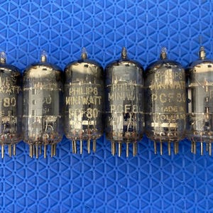 Puede incluir: Seis tubos de vacío Philips Miniwatt PCF80, con carcasas de vidrio y múltiples pines. Están dispuestos en fila sobre un fondo azul texturizado. El texto "MADE IN HOLLAND" es visible en algunos.