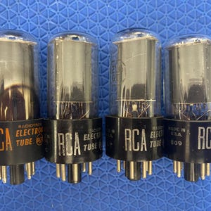 May include: Four vintage RCA Electron Tube vacuum tubes. Each tube has a clear glass bulb and a black base with the RCA logo and "Electron Tube" printed on it. The tubes are on a blue surface.
