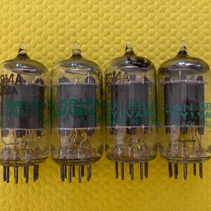 May include: Four vintage vacuum tubes with clear glass bulbs and black internal components. Each tube has the text "5814A USA" and "JAN 5814 SYLVANIA MADE IN USA" printed in green. The tubes are arranged in a row against a yellow background.