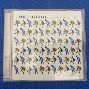 Könnte beinhalten: Eine transparente CD-Hülle aus Kunststoff mit dem Albumcover von The Police, Every Breath You Take, The Classics. Das weiße Cover zeigt ein sich wiederholendes Rastermuster aus kleinen, stilisierten Figuren in abwechselndem Blau und Gelbgrün.