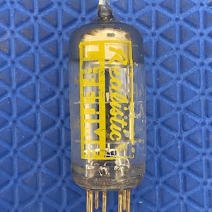 May include: A clear glass vacuum tube with a yellow label that reads "Realistic". The tube has a pointed top and several gold-colored pins at the base. The background is a blue, geometric pattern.
