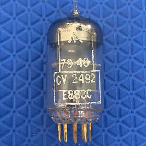 May include: A clear glass vacuum tube with a metallic top and gold-coloured pins. The tube has printed text including "79-46", "CV 2492", and "E88CC". This electronic component is likely from vintage audio equipment.