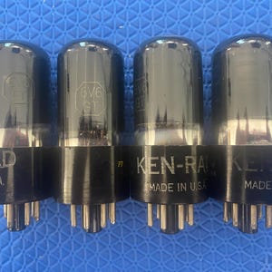 May include: Four vintage vacuum tubes with black bases and clear glass tops. The tubes are labeled "RAD" and "KEN-RAD", with "MADE IN U.S.A." printed on the bases. The model number "6V6 GT" is visible on some tubes.