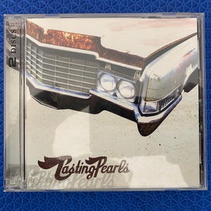 May include: A CD case featuring the album "Lasting Pearls." The cover art showcases a vintage car's front end with a rusted hood. The album title is in a stylized font. The case indicates it contains two discs.