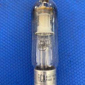 May include: A clear glass RCA Radiotron 872A electron tube with a silver metal base. The tube features internal wire components, a white ceramic-like structure, and black printed text on the glass and base, including the model number 872A.