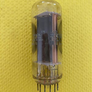 Puede incluir: Un tubo de vacío vintage con una carcasa de vidrio transparente, con componentes internos de cobre y negro. El tubo tiene múltiples pines en la base y el texto "COOL M. REG. MADE IN JAPAN".