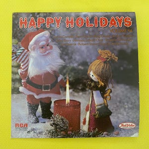 May include: A vintage album cover titled "Happy Holidays Volume 14" featuring Santa Claus and a doll figurine. A lit red candle is between them. The RCA and True Value logos are visible.
