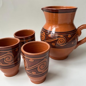 May include: A set of four terracotta drinking cups and a pitcher with brown and orange swirl designs.