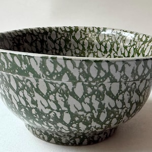 May include: A ceramic mixing bowl featuring a white base color with a dark green sponge-painted or mottled pattern across the entire exterior and interior surface. The bowl has a wide, rounded rim and a slightly tapered base for stability.