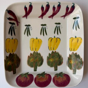 Pode incluir: Uma travessa retangular de cerâmica com fundo creme. A travessa é decorada com ilustrações coloridas de vegetais, incluindo pimentas vermelhas, pimentões amarelos, alcachofras e tomates. O design é um estilo caprichoso, pintado à mão.