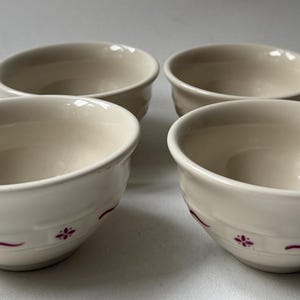 Op de afbeelding: Een set van vier gebroken witte keramische kommen gerangschikt in een vierkante formatie. Elke kom heeft een gladde, afgeronde rand en een decoratieve band rond de buitenste basis, bestaande uit kleine kastanjebruine bloemmotieven.