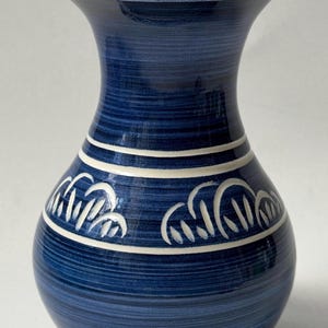 May include: A blue ceramic vase with a wide base and a flared rim. The vase features a textured surface with horizontal lines and white decorative patterns. The vase is approximately 10 inches tall.