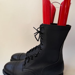 Puede incluir: Botas de combate de cuero negro con diseño de cordones. Las botas tienen una puntera redondeada y una suela resistente. Hormas rojas se insertan dentro de las botas para mantener su forma. Estas botas están diseñadas para la durabilidad y la protección.
