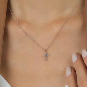 K&ouml;nnte beinhalten: Eine zarte Silberkette mit einem kleinen Kreuzanh&auml;nger, der mit funkelnden Edelsteinen besetzt ist. Das Kreuz ist an einer feinen Kette befestigt und erzeugt ein schlichtes, aber elegantes Design.